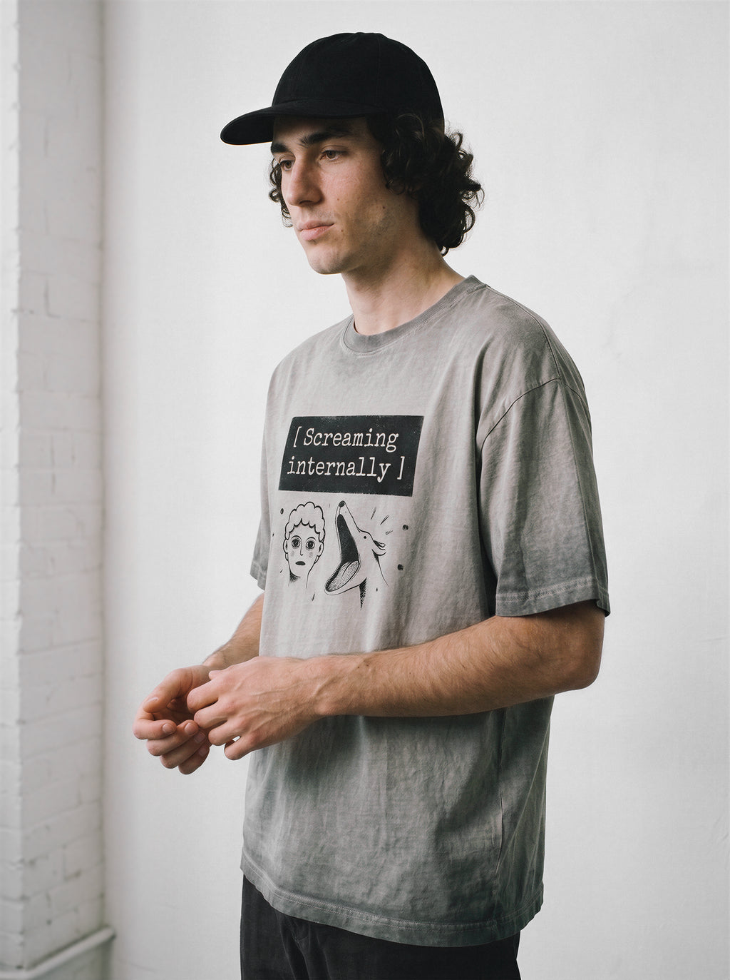 A male model looking away wearing an ombre grey screaming internally ironic graphic tee, capturing the existential streetwear style and mental health humor.