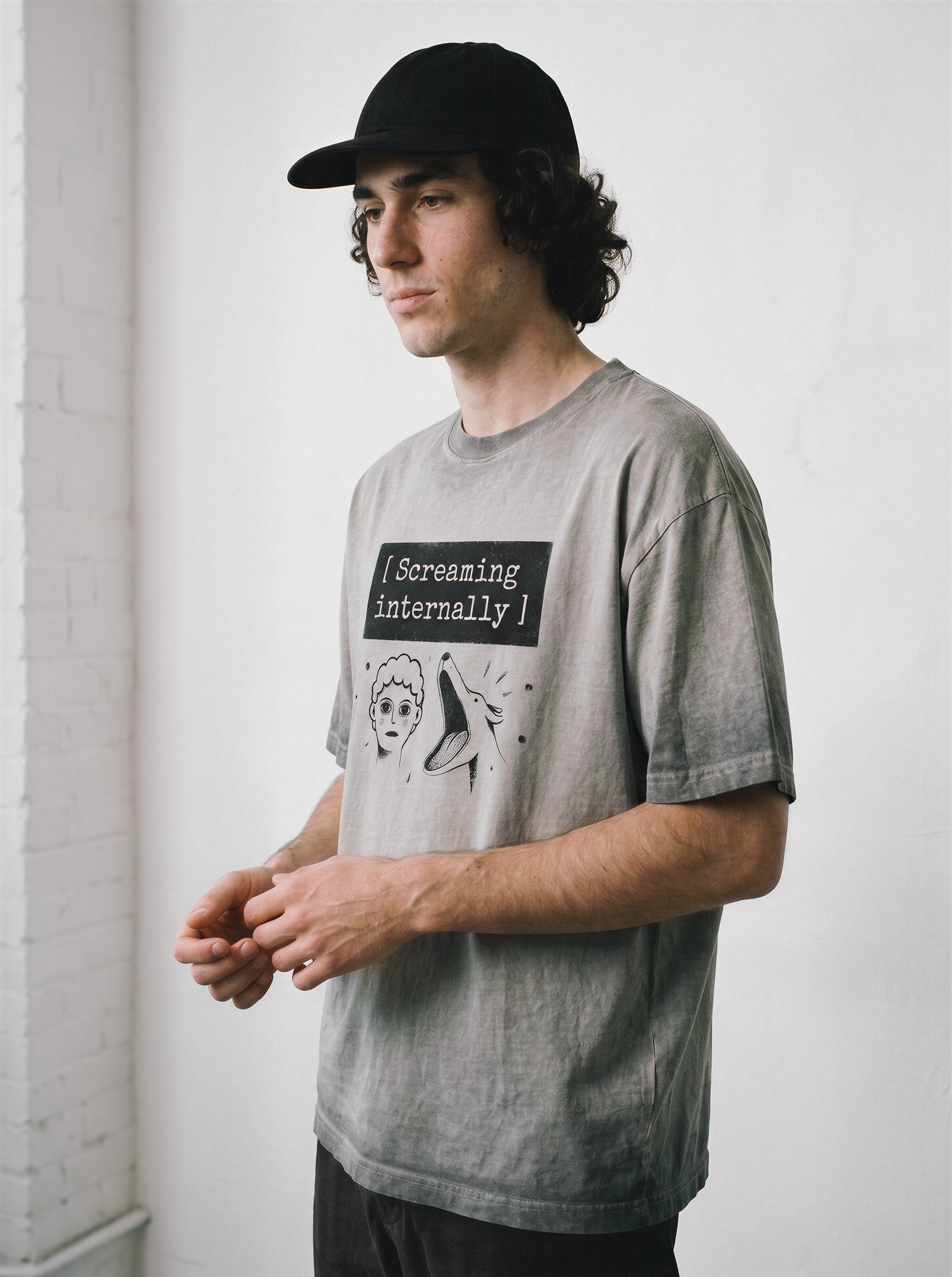 A male model looking away wearing an ombre grey screaming internally ironic graphic tee, capturing the existential streetwear style and mental health humor.