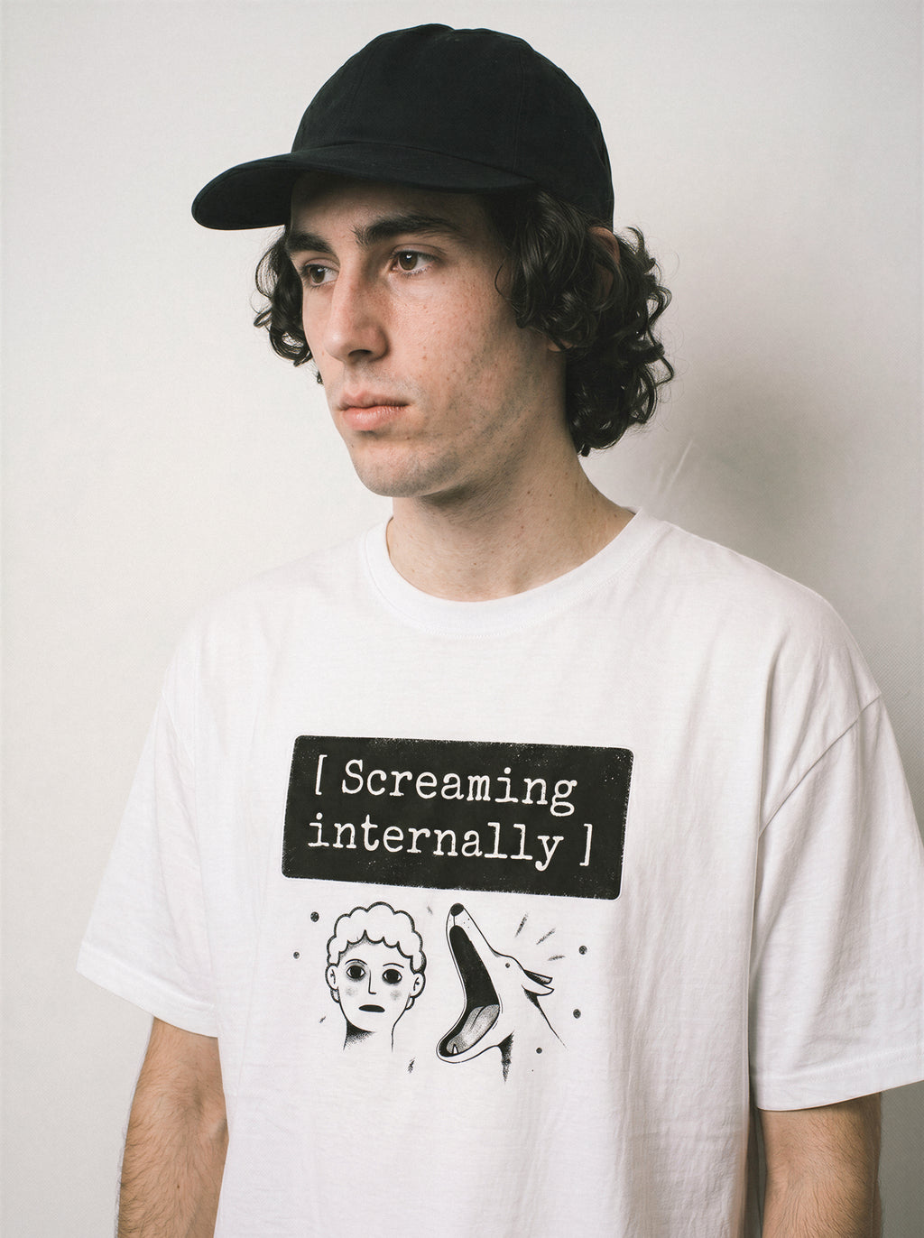 A side stance of a male model wearing a white screaming internally psychological graphic tee, emphasizing the silent breakdown concept and casual drape.