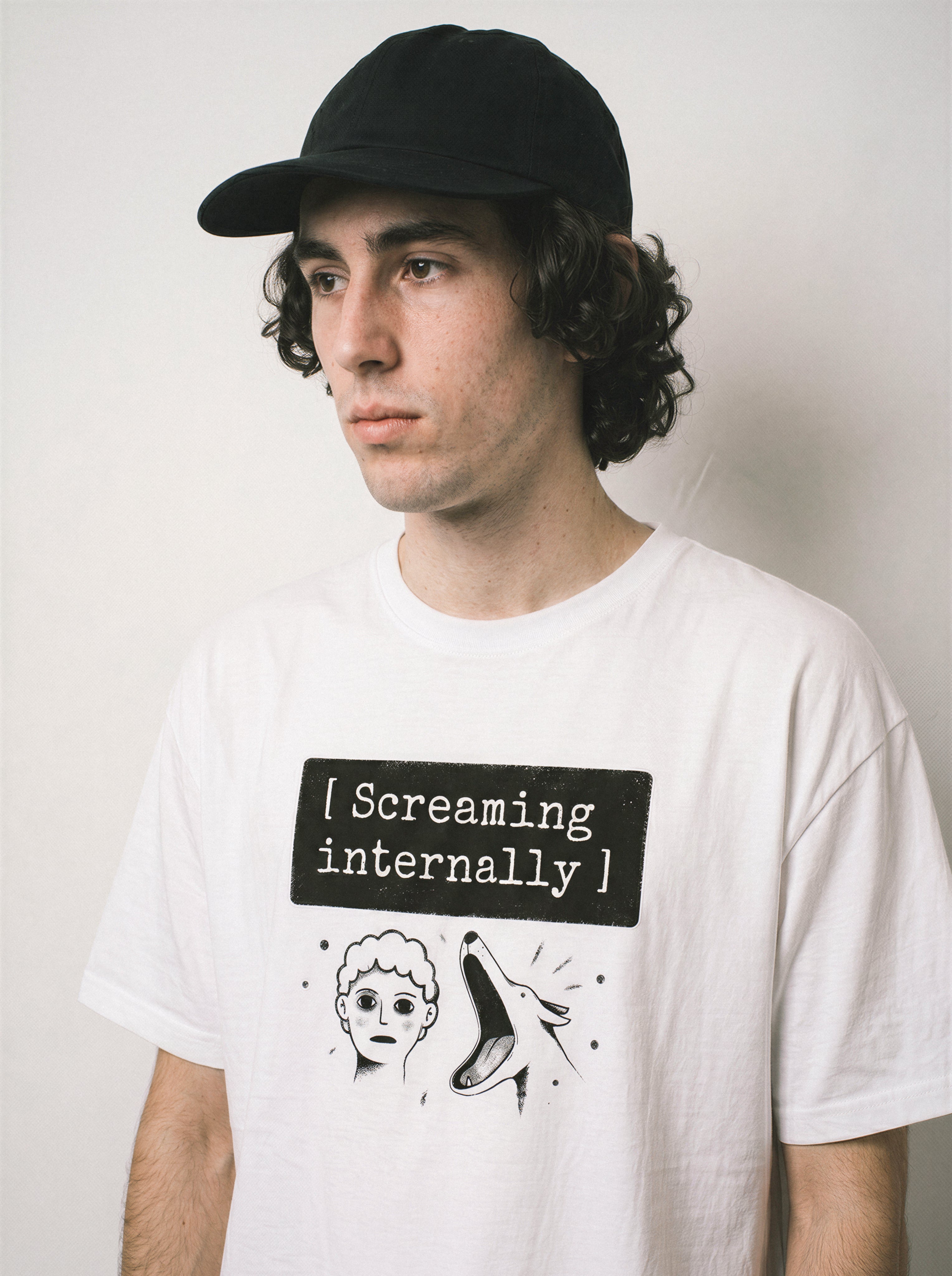 A side stance of a male model wearing a white screaming internally psychological graphic tee, emphasizing the silent breakdown concept and casual drape.