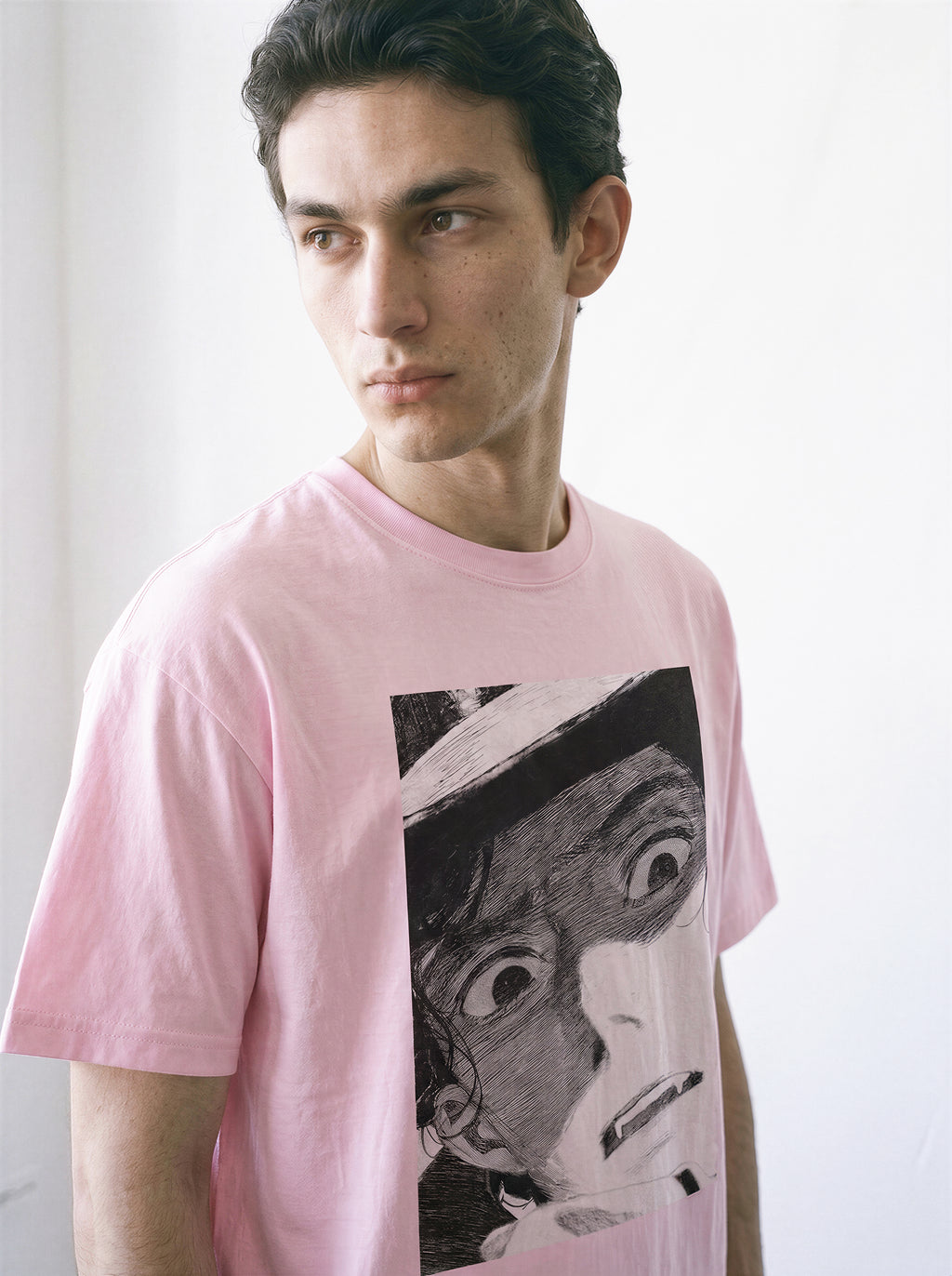 A male model looking away wearing a light pink shocked face manga panel graphic tee, highlighting the bold independent manga aesthetic and casual streetwear style.