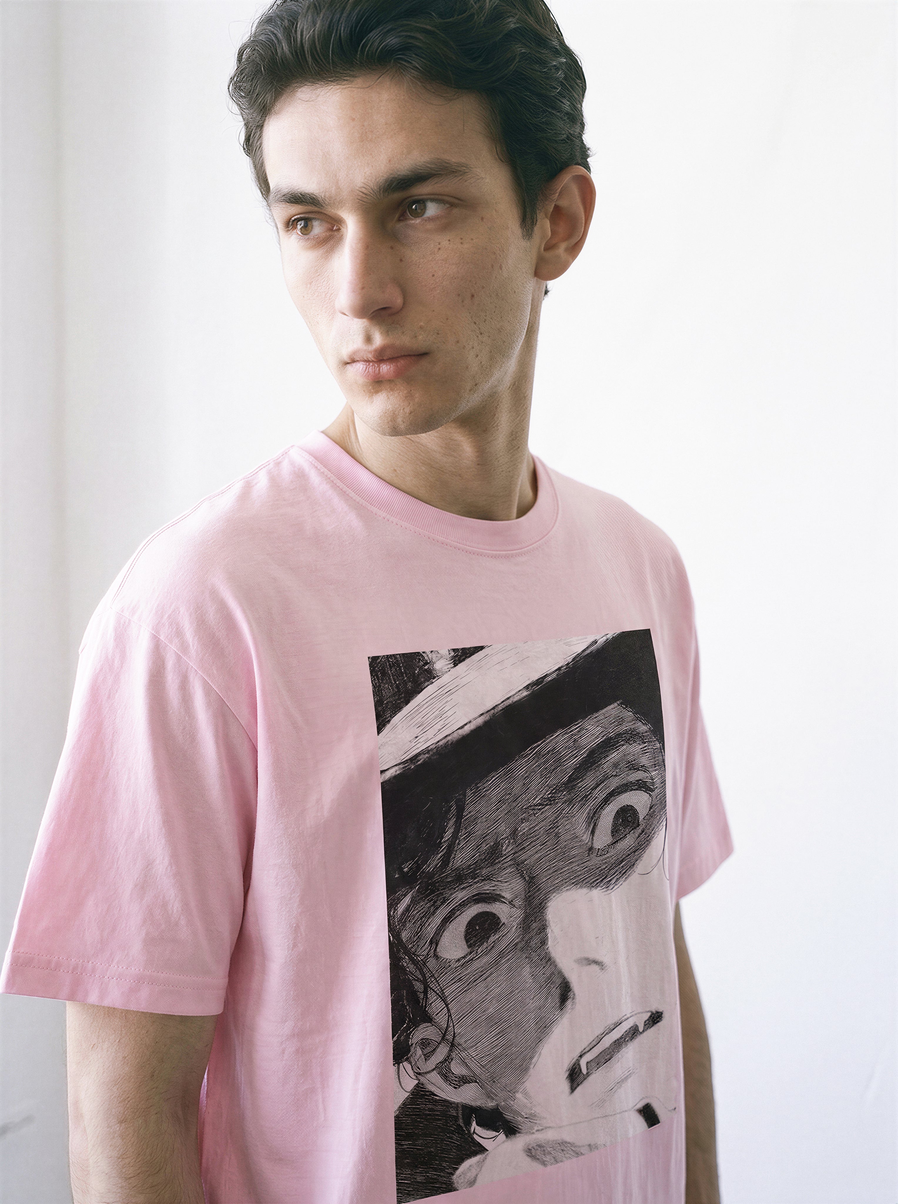 A male model looking away wearing a light pink shocked face manga panel graphic tee, highlighting the bold independent manga aesthetic and casual streetwear style.