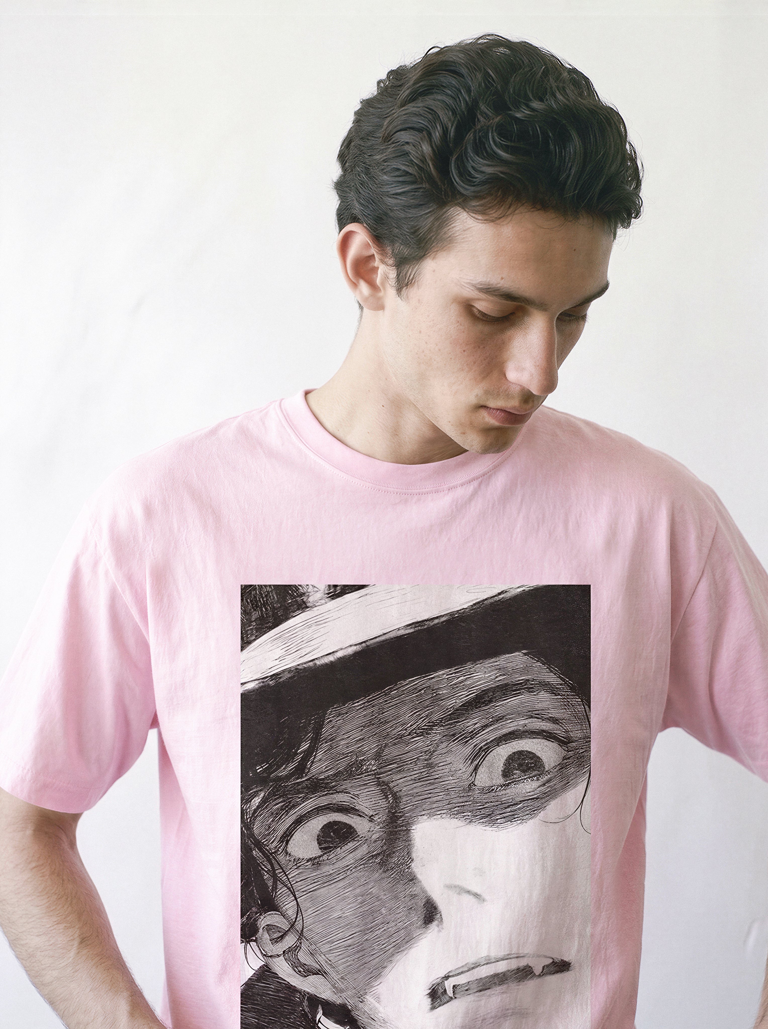 A male model looking down wearing a light pink shocked face manga panel graphic tee, emphasizing the raw emotion of the striking monochrome print.