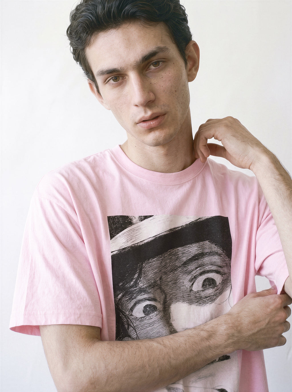A male model touching his neck wearing a light pink shocked face manga panel graphic tee, capturing a nostalgic streetwear vibe with a vintage anime graphic.
