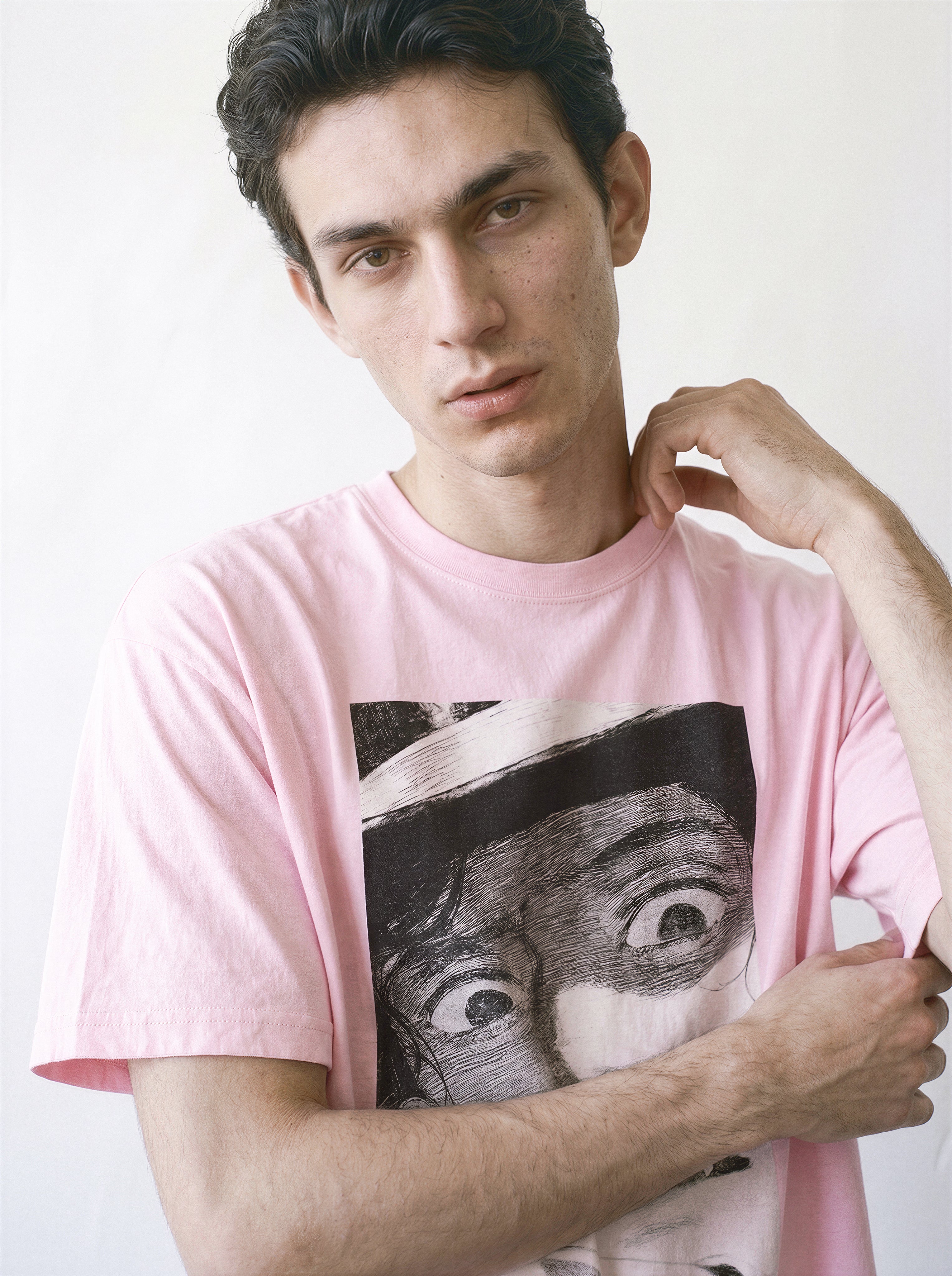 A male model touching his neck wearing a light pink shocked face manga panel graphic tee, capturing a nostalgic streetwear vibe with a vintage anime graphic.