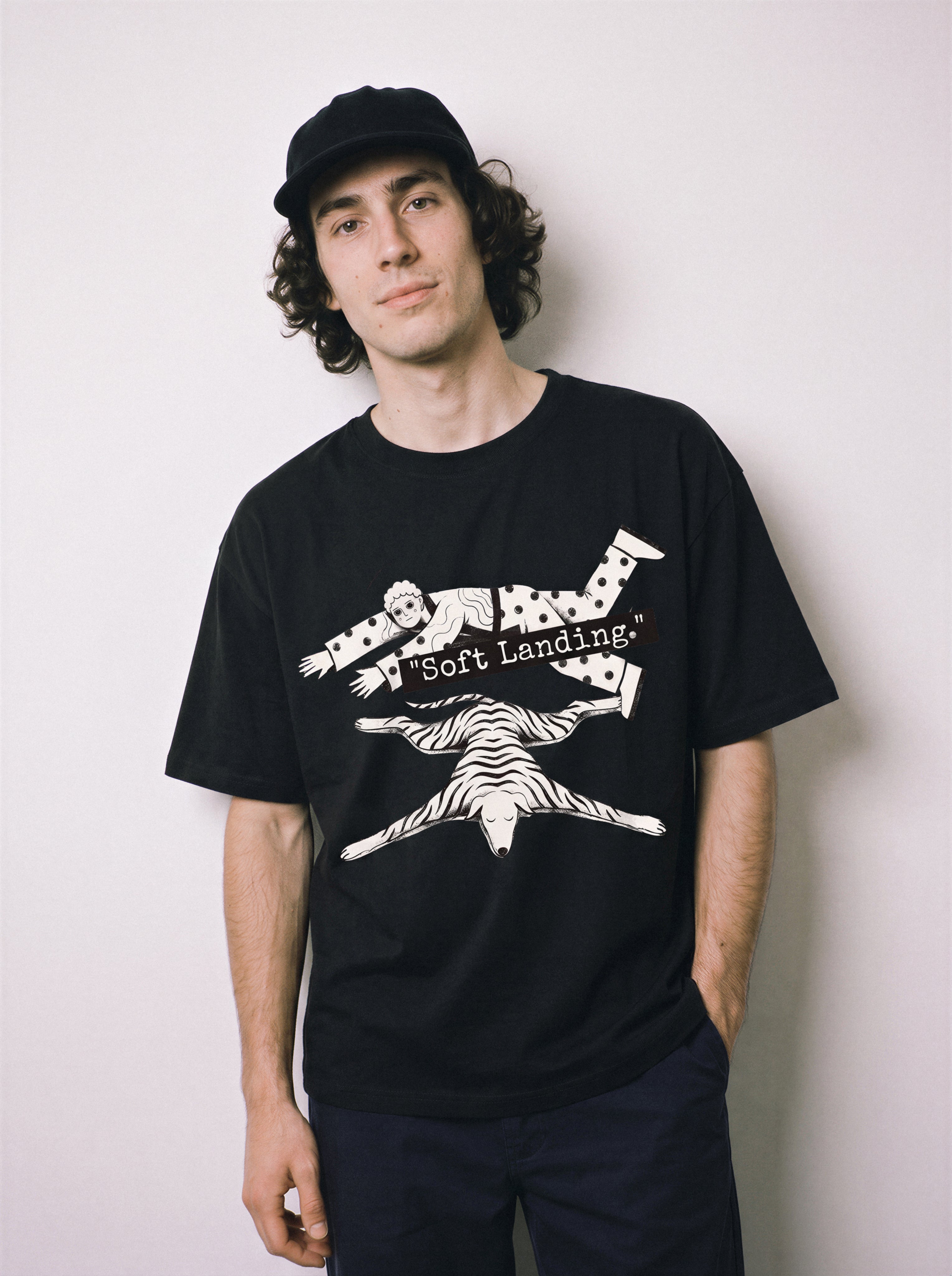 A male model with hands in pockets standing wearing a black soft landing line art graphic tee, highlighting the promised economic miracle vibe and relaxed boxy fit.