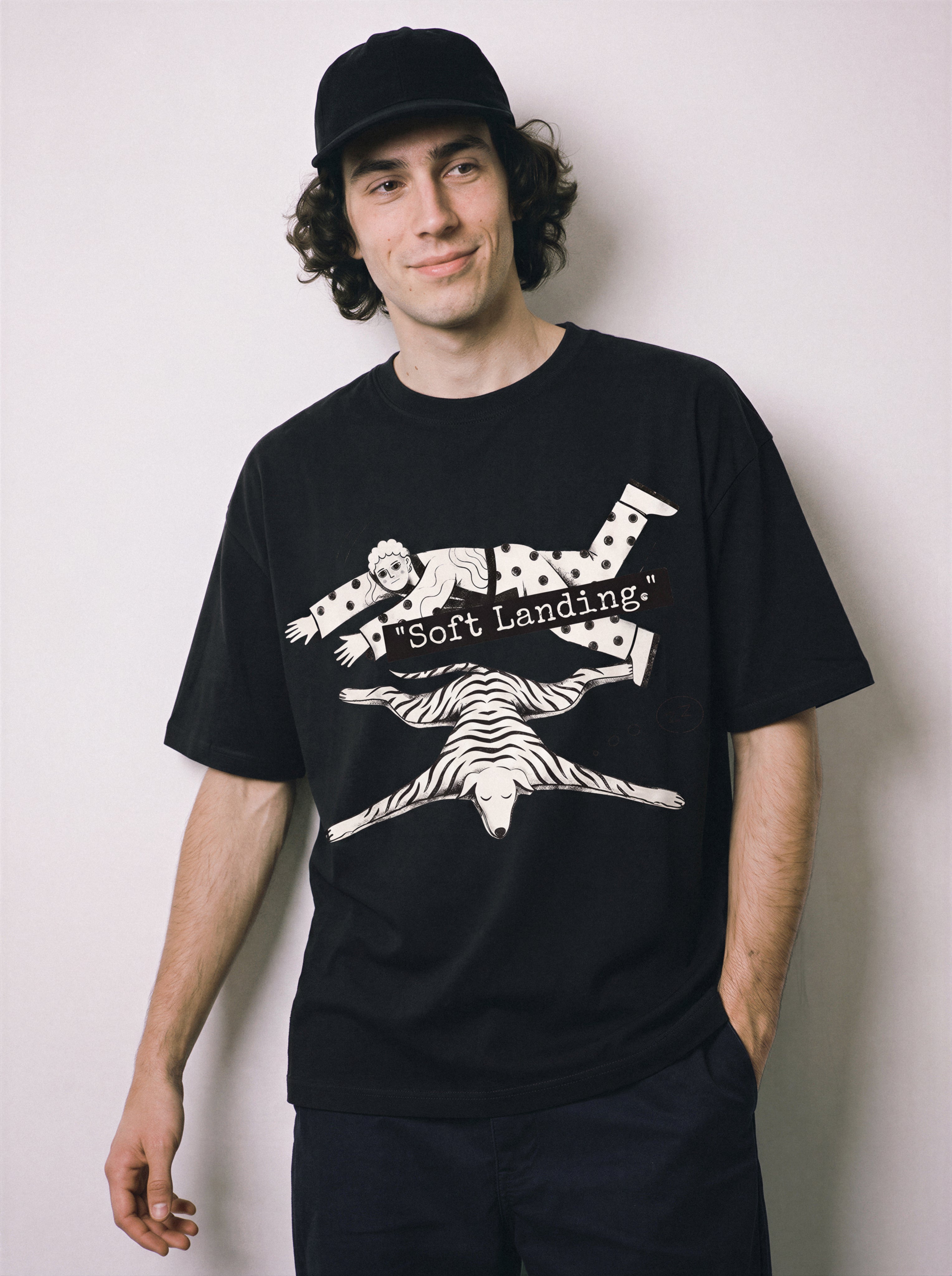 A male model smiling with arms down wearing a black soft landing line art graphic tee, emphasizing the satirical economic joke and casual drape.
