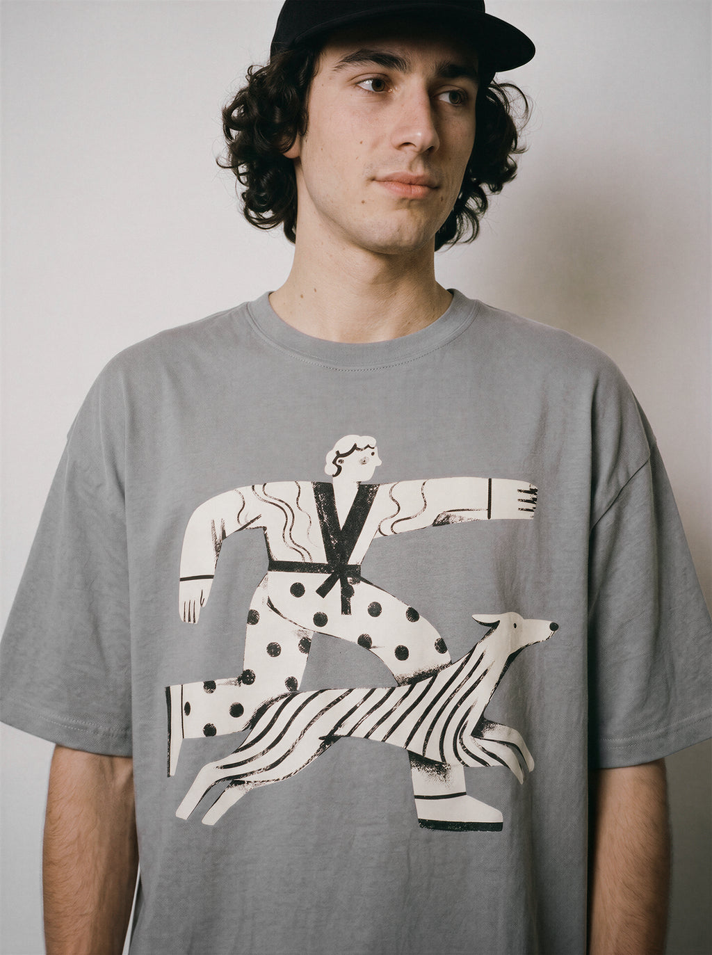 A close-up of a male model wearing a gray striding away line art graphic tee, showcasing the person and dog striding forward with absolute conviction.