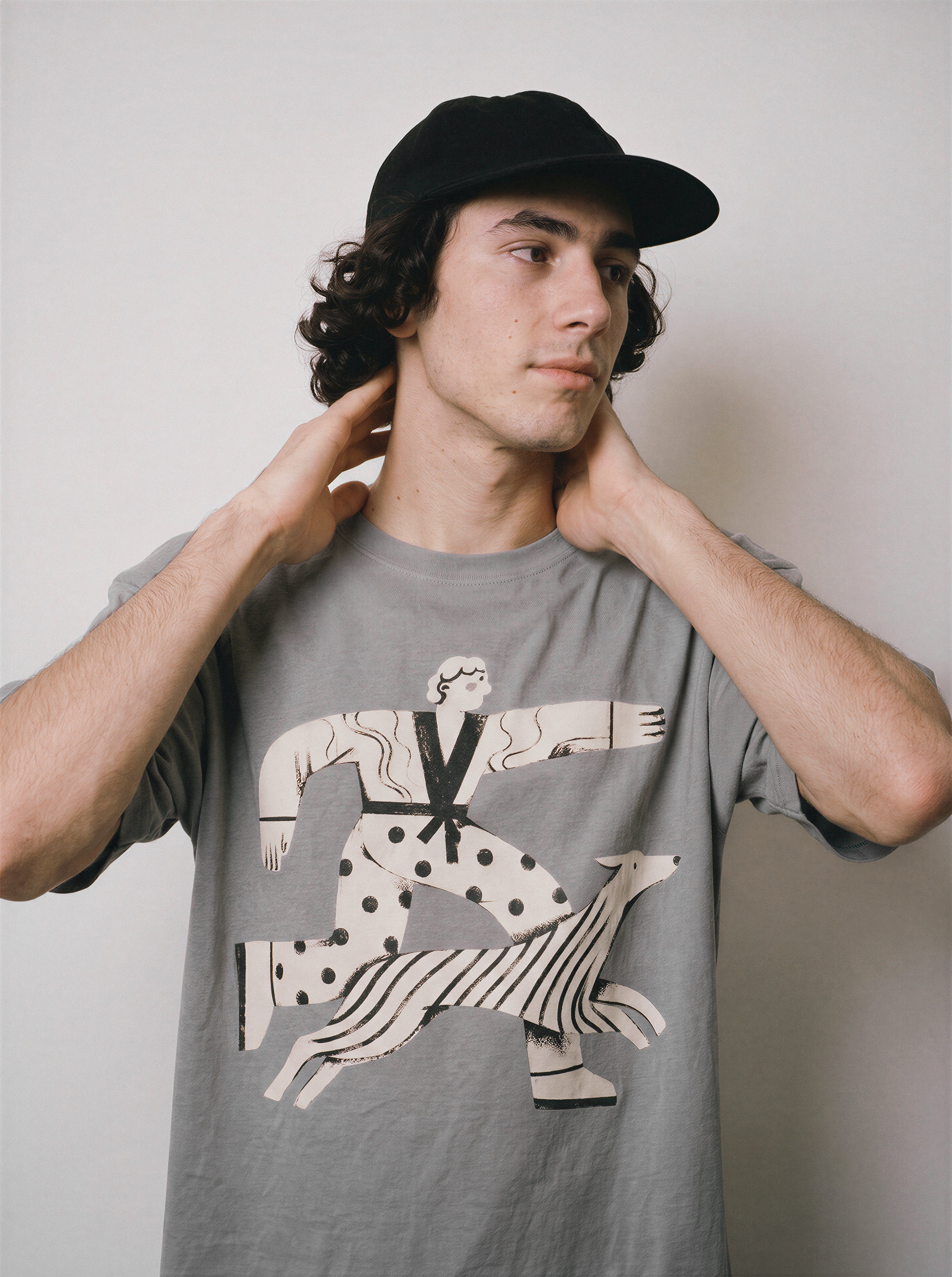 A male model with hands behind his neck wearing a gray striding away line art graphic tee, capturing the unbothered aesthetic and strutting past the drama vibe.