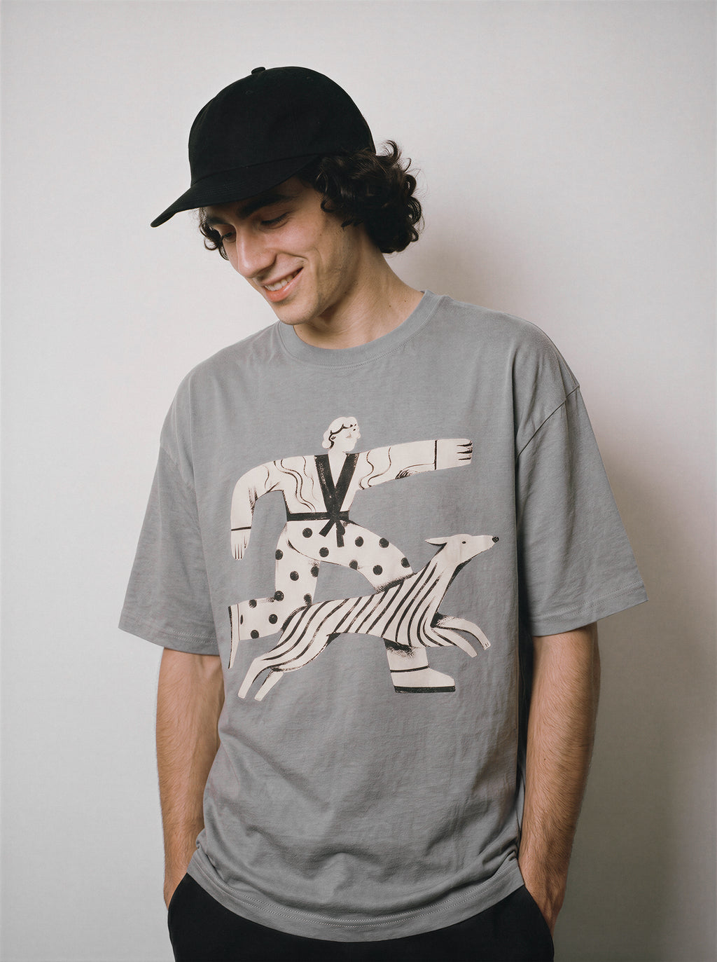 A male model with hands in pockets wearing a gray striding away line art graphic tee, emphasizing the pure line art form and casual everyday drape.