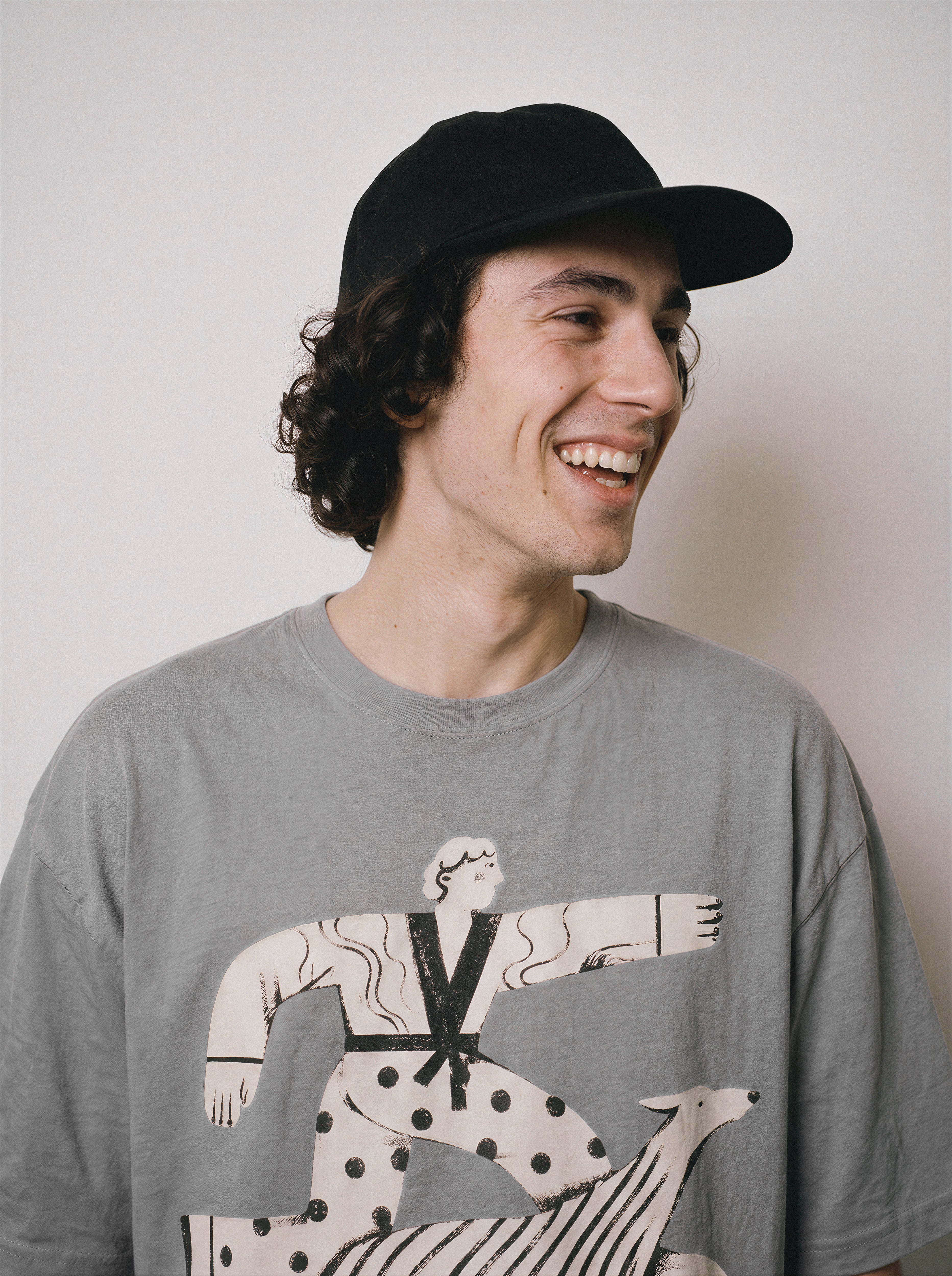 A profile portrait of a smiling male model wearing a gray striding away line art graphic tee, focusing on the detached streetwear style and lighthearted mood.