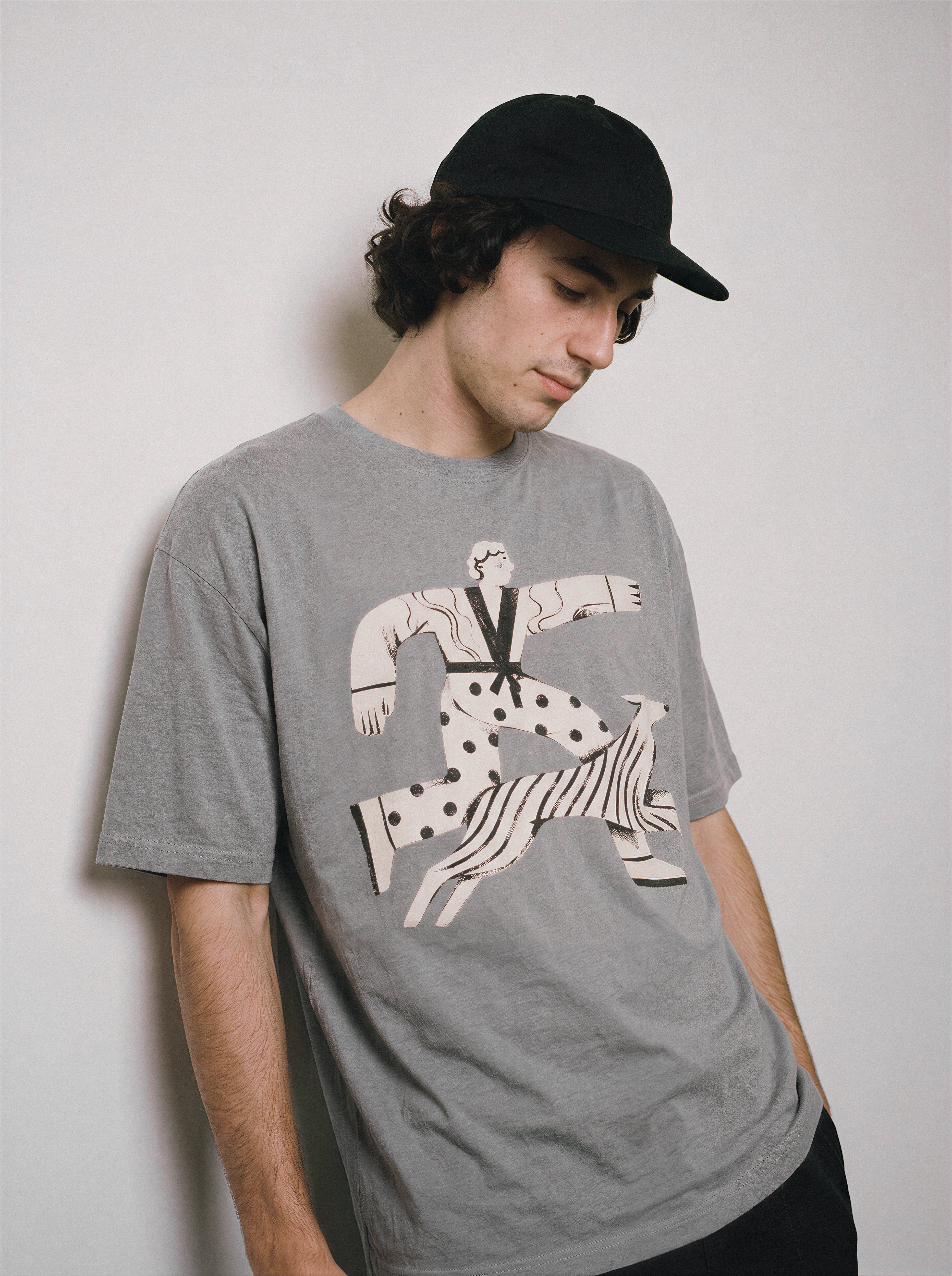 A male model standing sideways wearing a gray striding away line art graphic tee, highlighting the fabulous exit mindset and relaxed boxy fit.