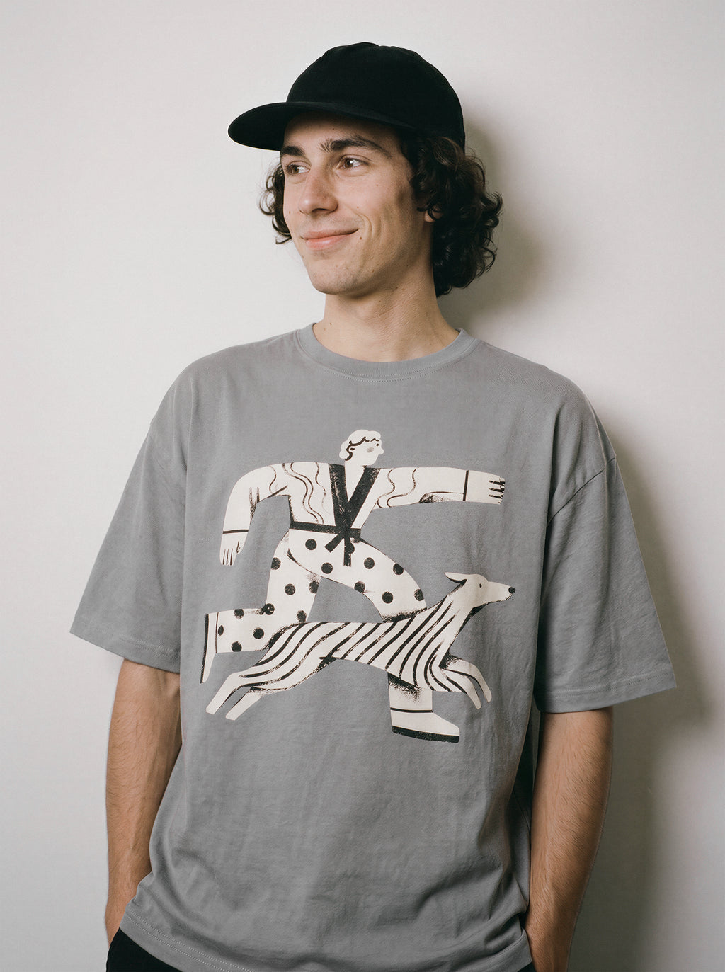 A male model smiling and looking right wearing a gray striding away line art graphic tee, conveying the conviction mindset that problems can't catch me.