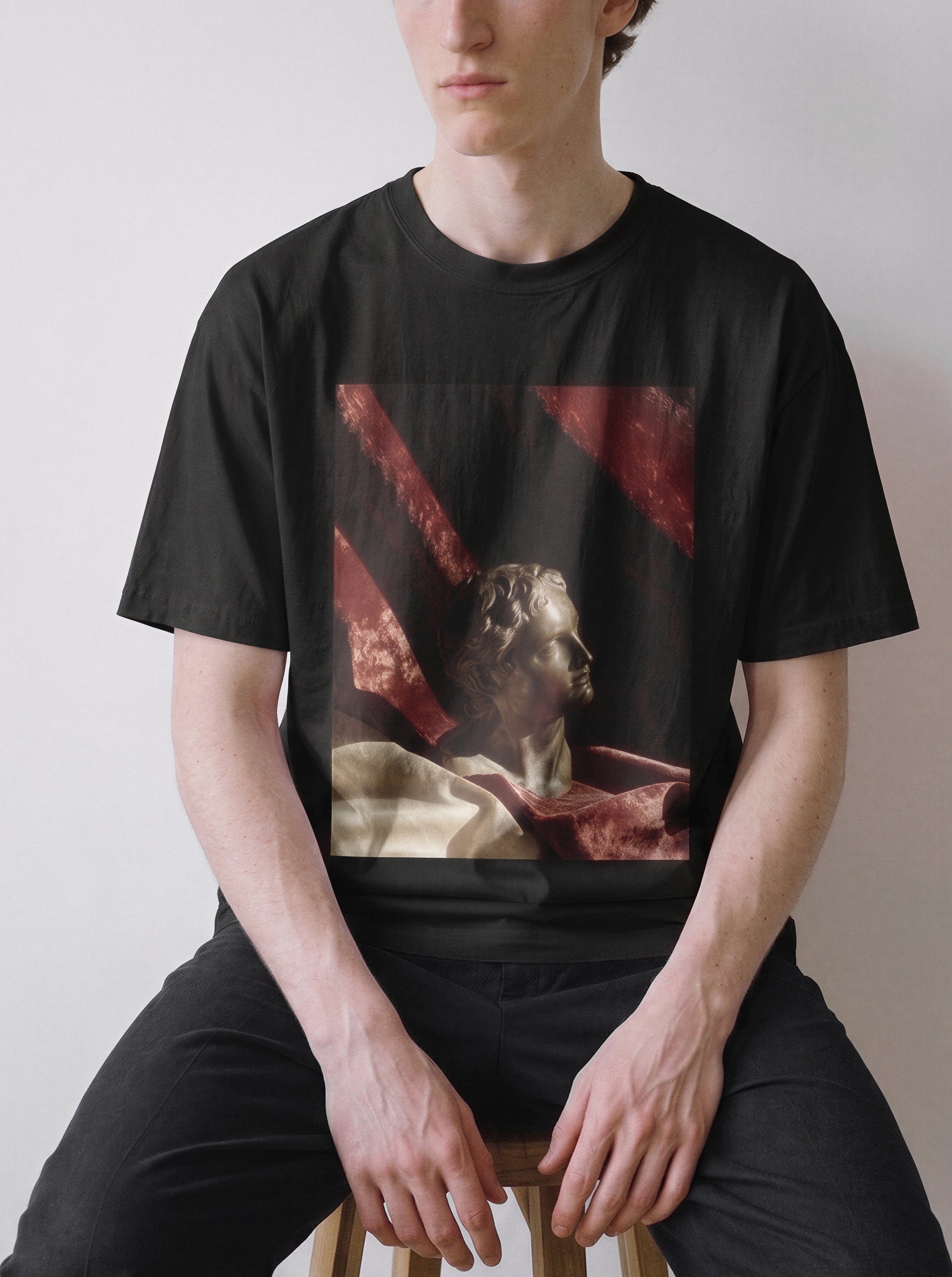 A seated male model with hands on his thighs wearing a black surreal classical bust graphic tee, capturing the thought and silence concept through a bold sculpture graphic print.