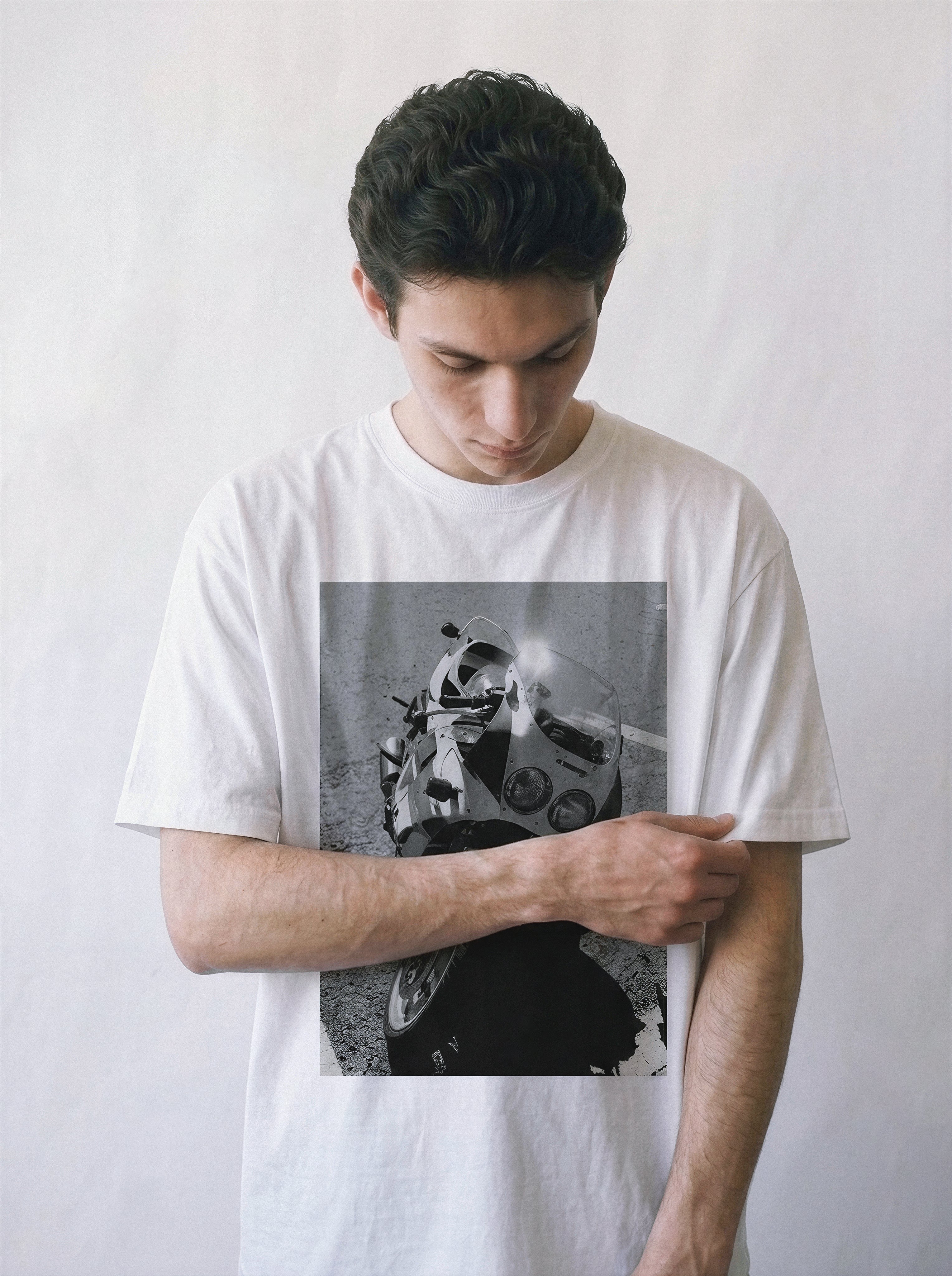 A male model adjusting his sleeve wearing a white 90s monochrome motorcycle photography tee, emphasizing the raw mechanical aesthetic and casual drape.