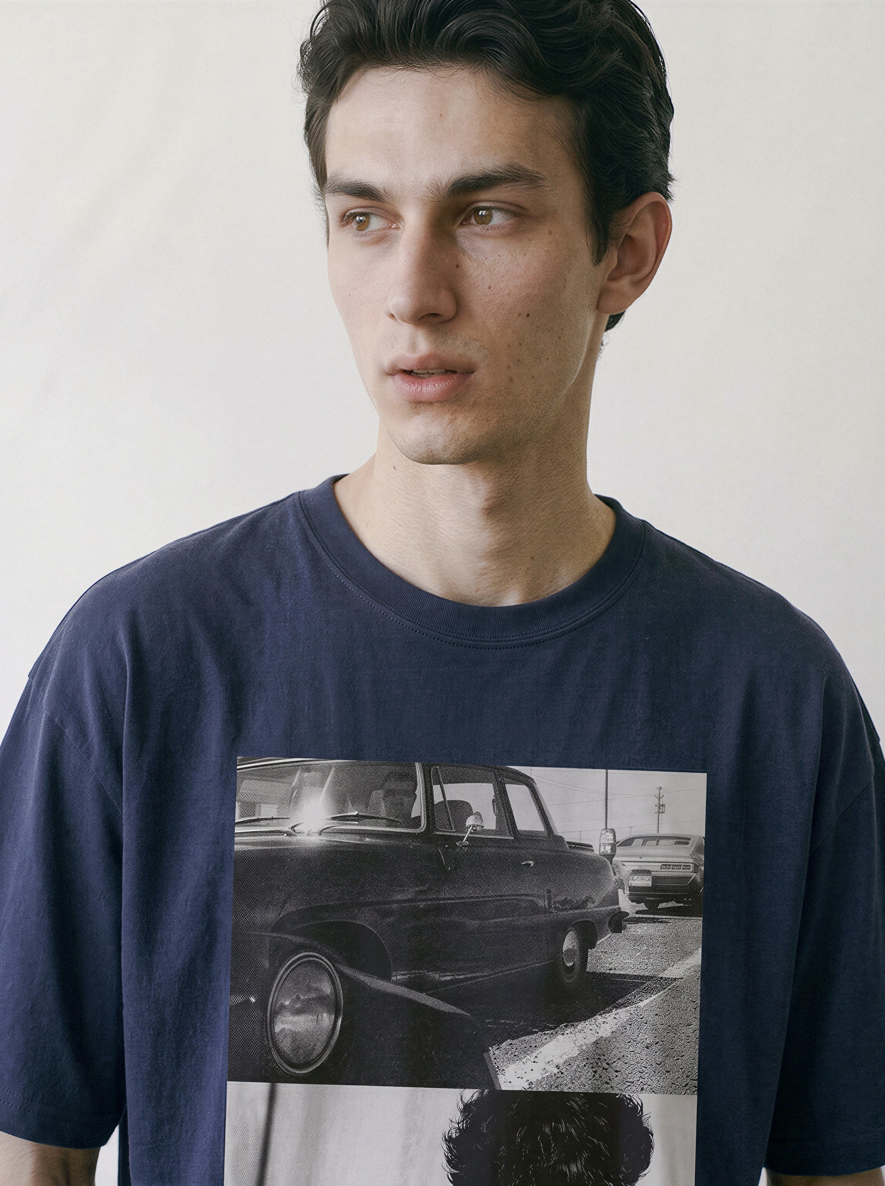 Chest-up view of a model looking to the right, wearing a vintage navy graphic t-shirt with a striking black and white 90s cinematic split-panel design.