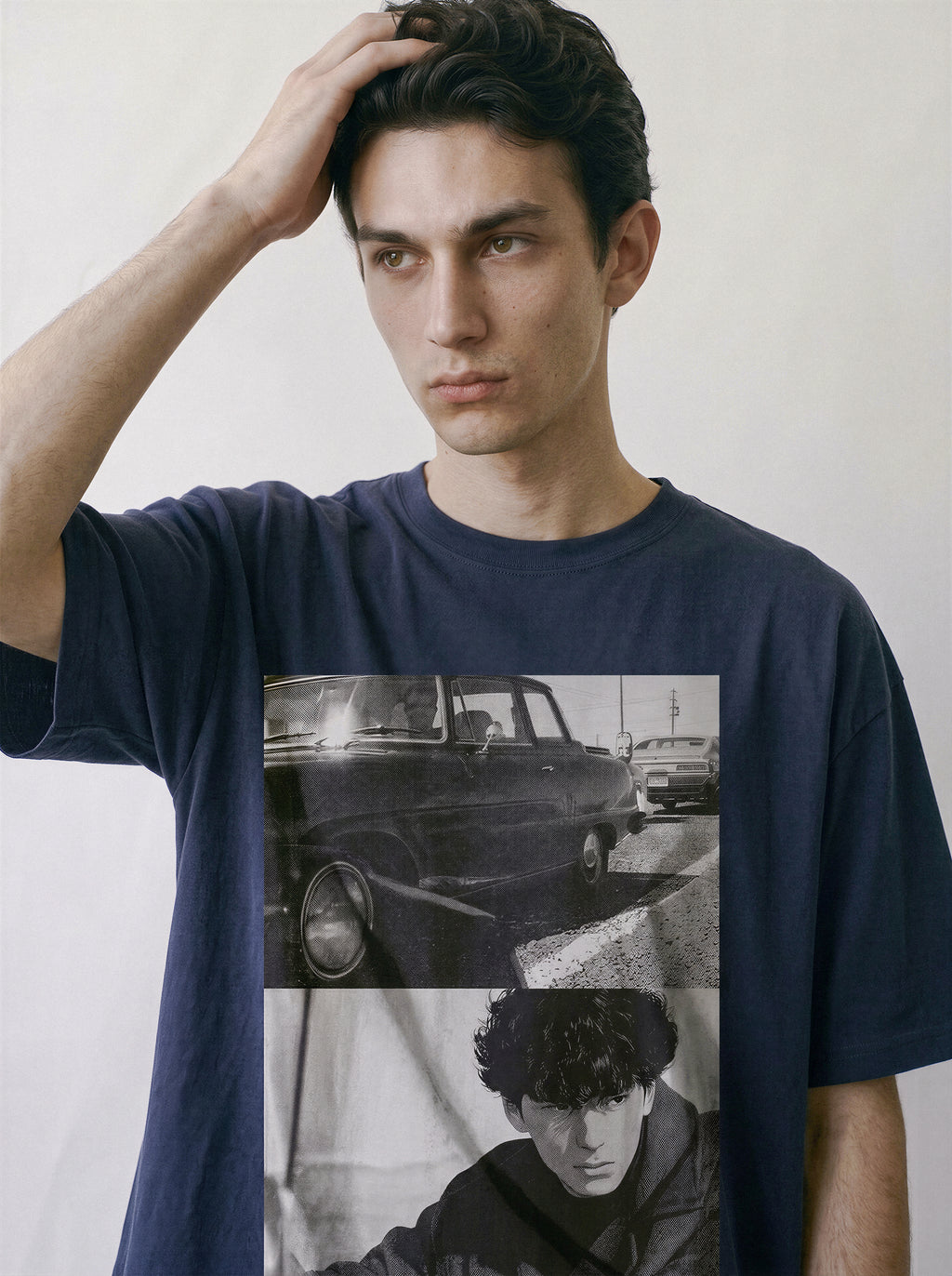 A male model resting his hand on his head, wearing a vintage navy 90s retro photography t-shirt featuring a gritty street realism car and silhouette print.