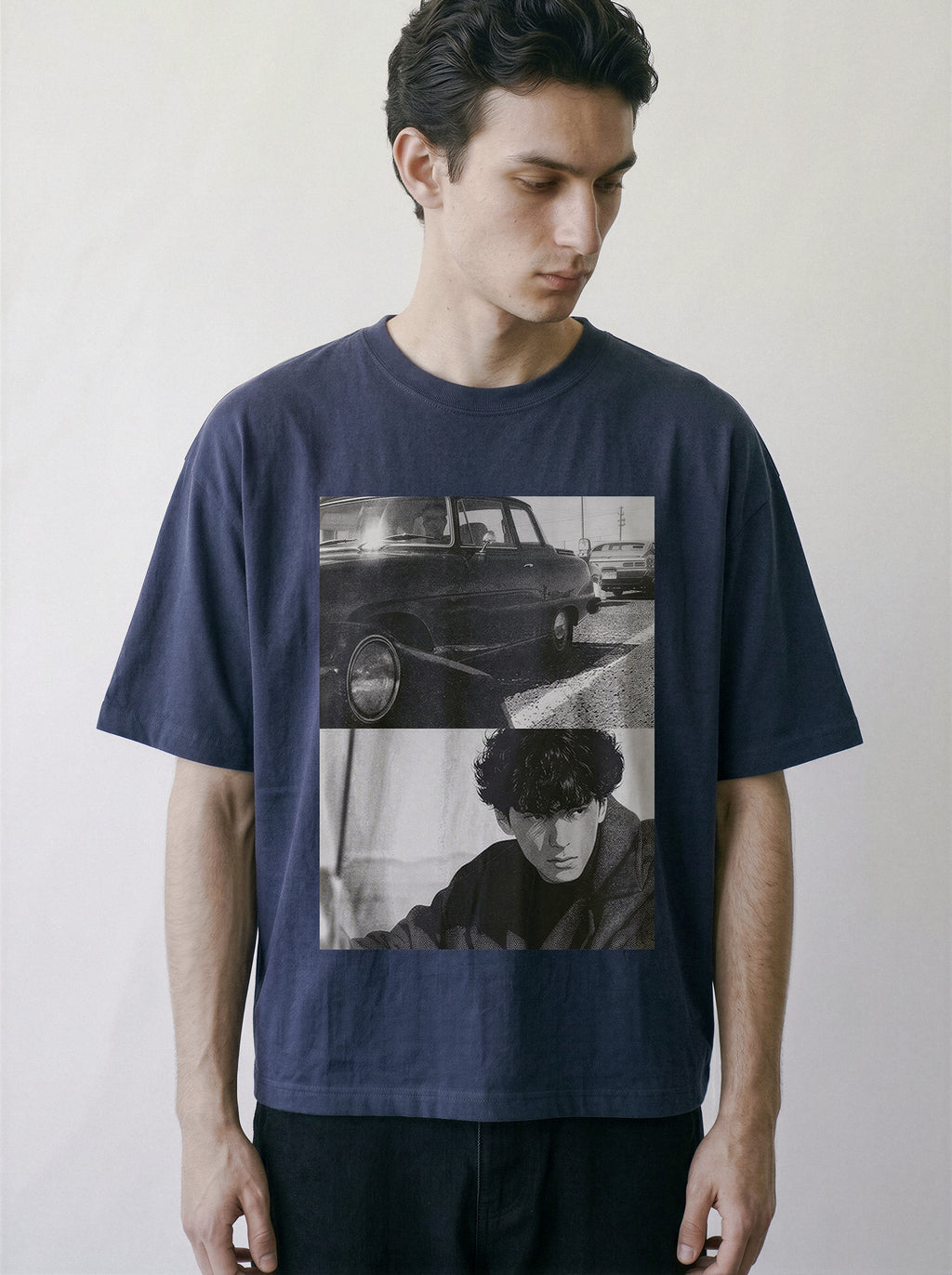 A man wearing a navy blue oversized graphic t-shirt with a black and white collage print of a vintage car and a portrait, set against a plain light gray background.