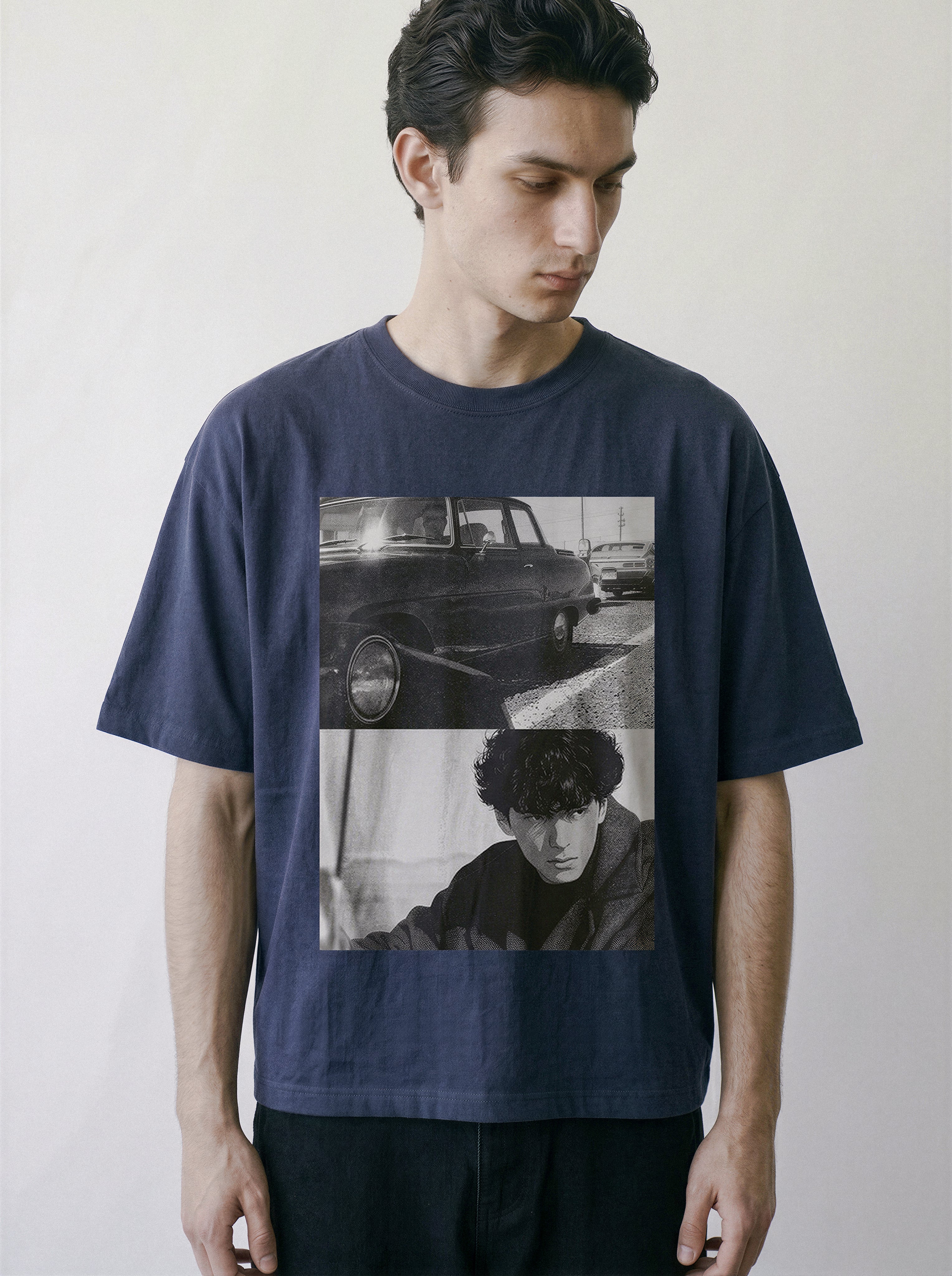 A man wearing a navy blue oversized graphic t-shirt with a black and white collage print of a vintage car and a portrait, set against a plain light gray background.