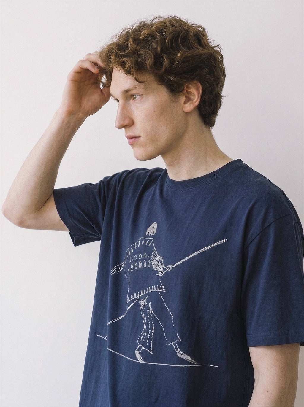 Side profile of a male model with his hand in his hair, wearing a vintage navy oversized graphic tee featuring a clean continuous line drawing of a tightrope walker.
