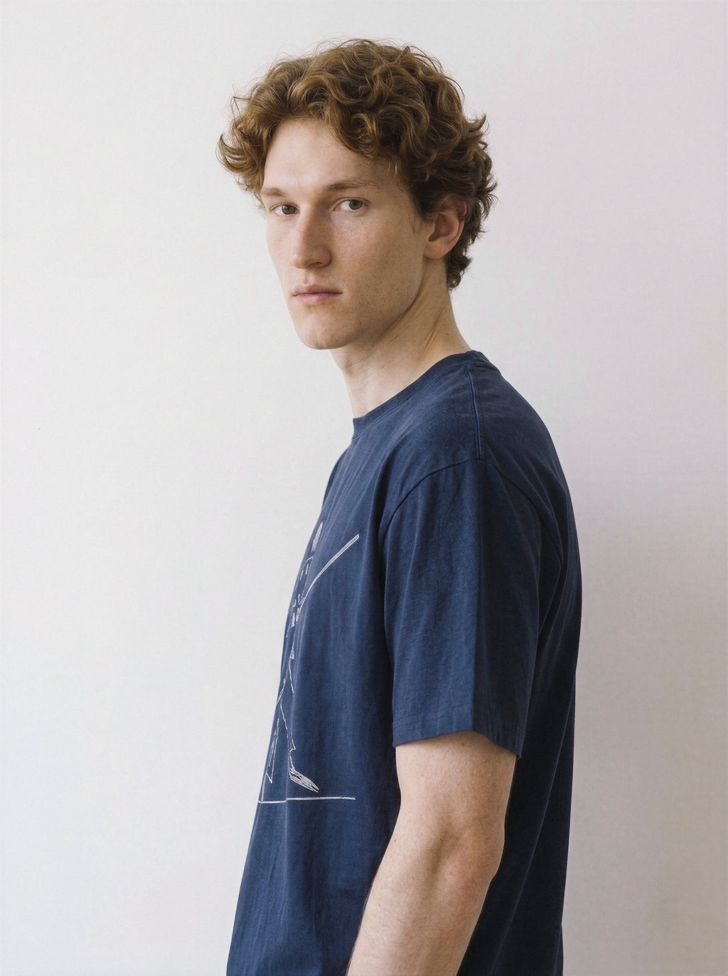 Side profile of a male model looking over his shoulder, wearing a vintage navy 180g premium cotton tee highlighting a minimalist tightrope walker print.