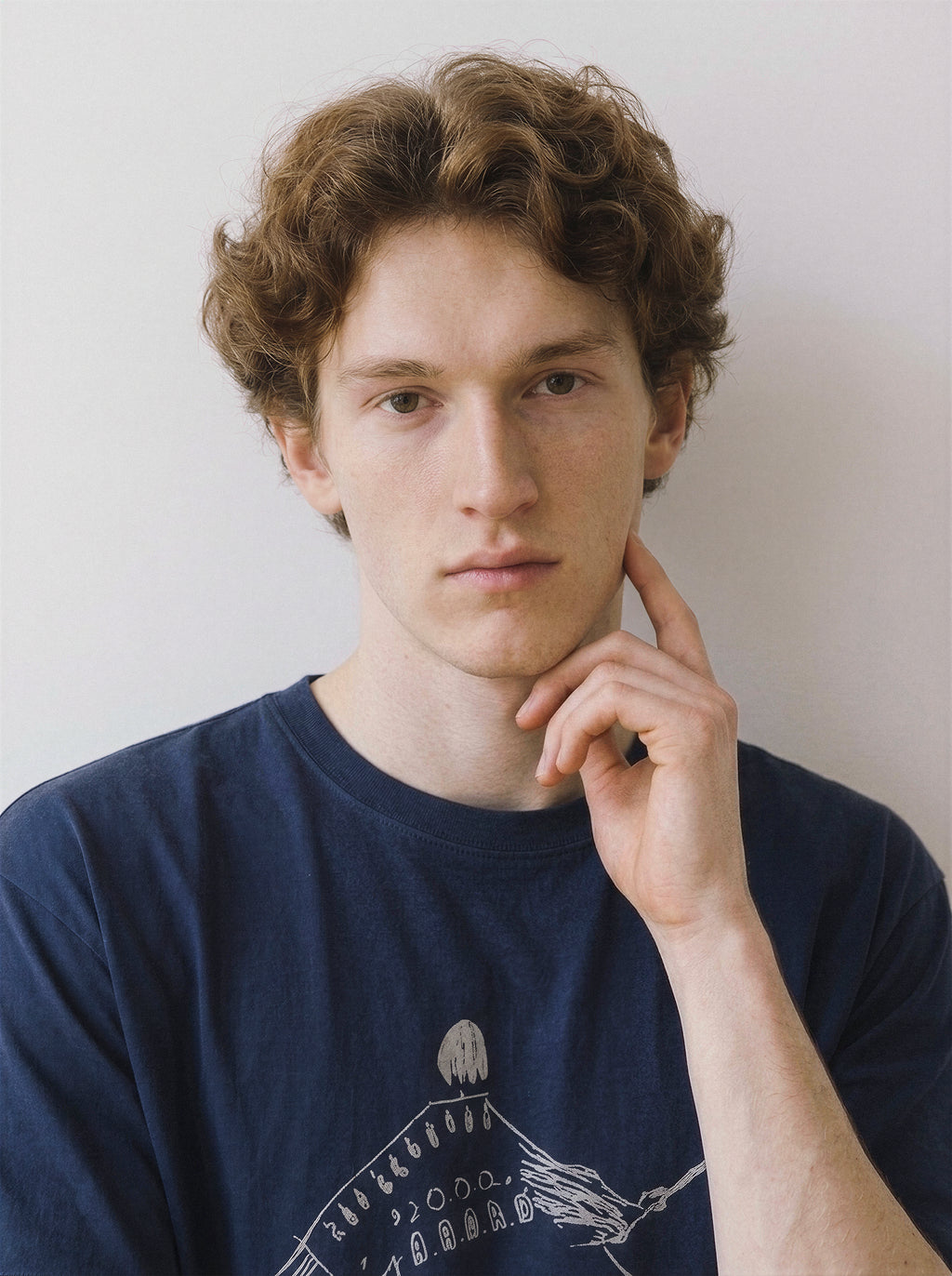 Close-up front portrait of a male model touching his chin, wearing a vintage navy oversized t-shirt with a striking tightrope walker line art illustration.