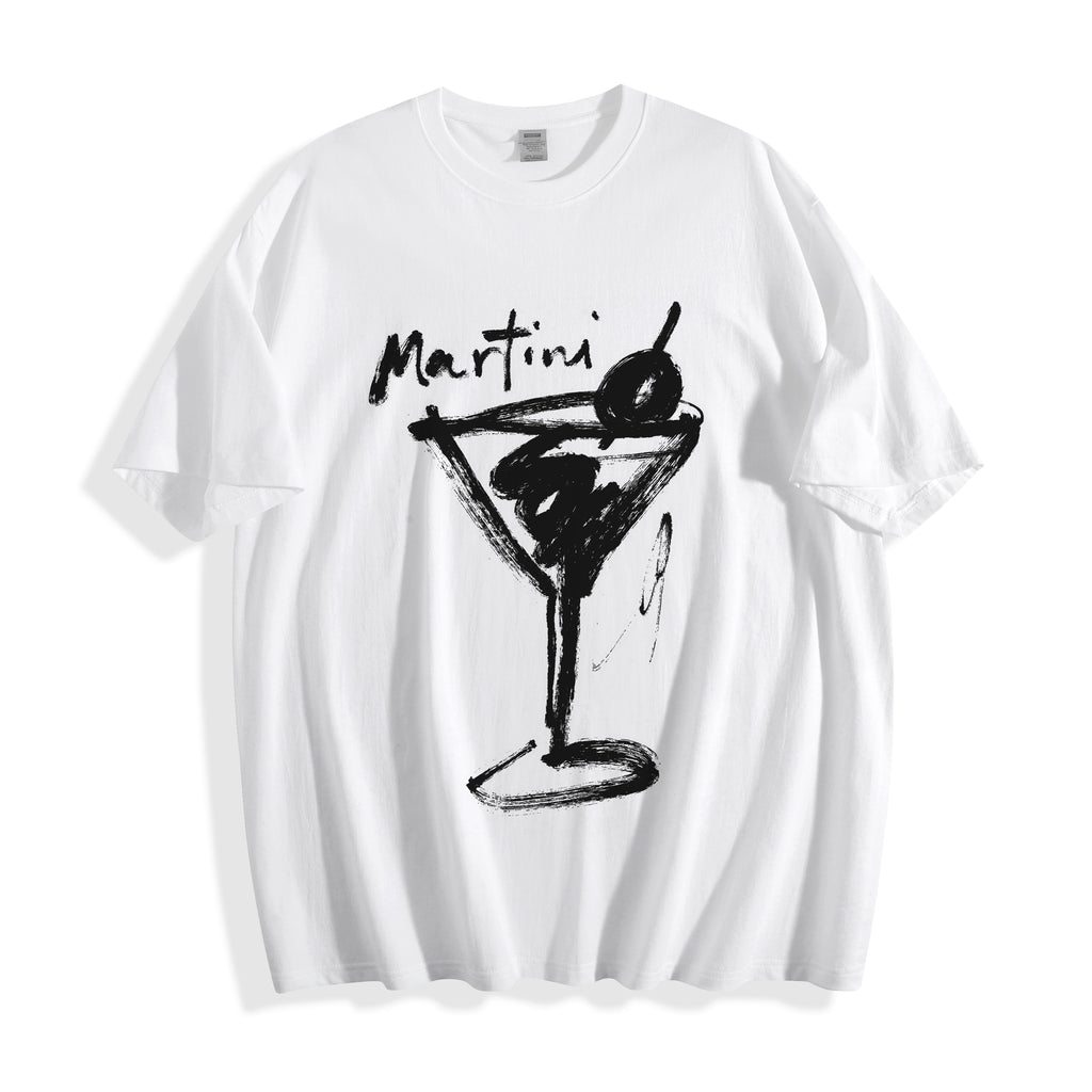Flat lay product photography of a crisp white t-shirt highlighting a high-contrast black brush-stroke martini line art print and the word 'Martini' written above it.