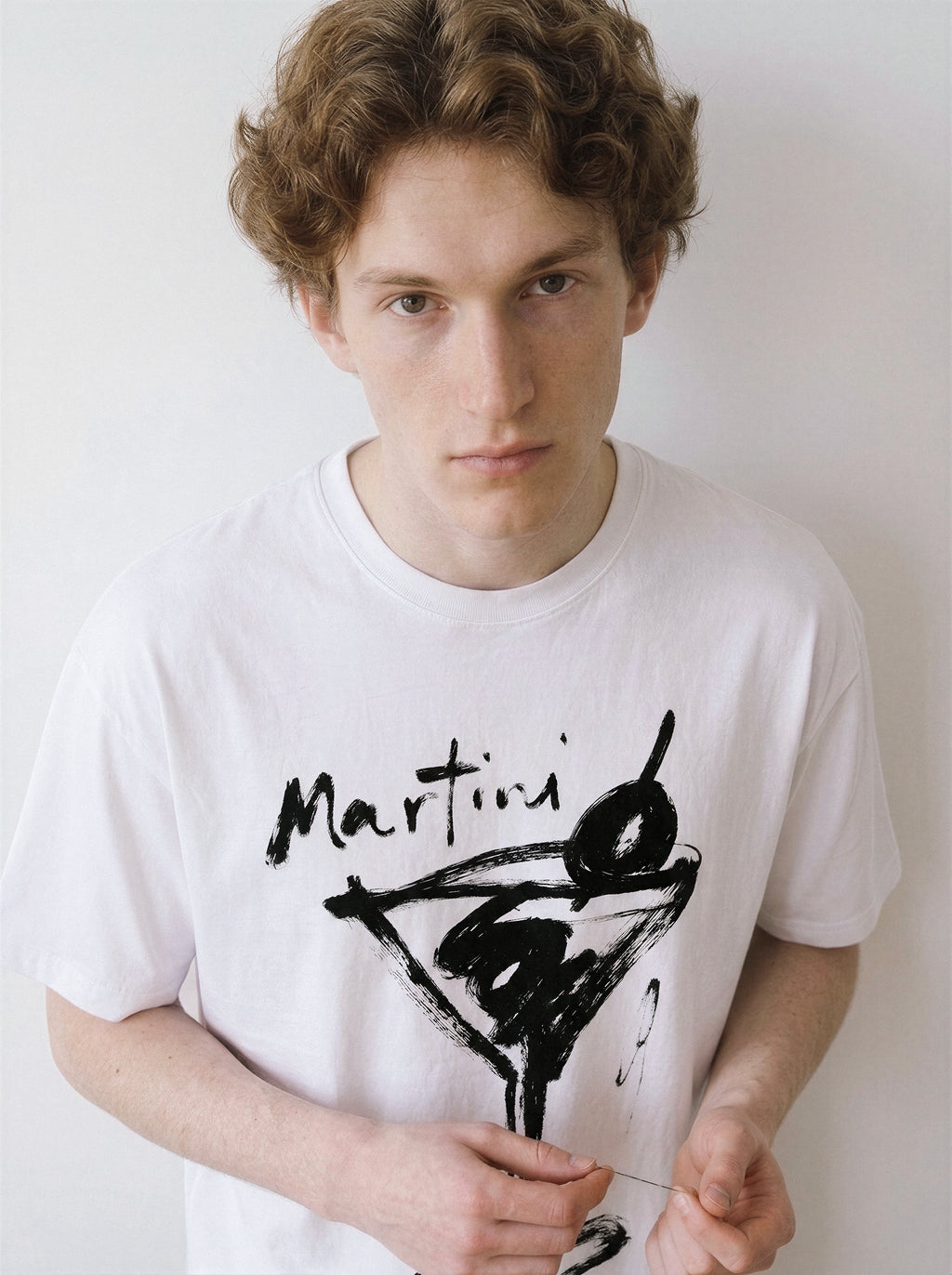 Front view of a male model looking directly at the camera, wearing a clean white graphic tee highlighting an expressive martini glass line art illustration.